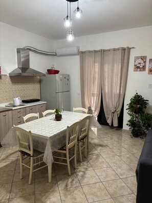 A kitchen with a dining table, chairs, a refrigerator, a stove, and a ceiling light fixture.