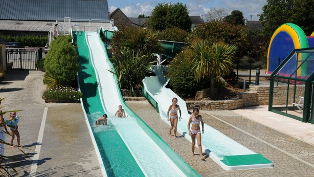 A water park with a long water slide, a pool, and a fenced area with trees and plants. - SEA VIEW HOUSE FACING GLENANSR ISLANDS (LA FORET-FOUESNANT)