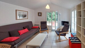 A living room with a sofa, two chairs, a coffee table, and a TV. There is a window with a view of greenery outside. - Beautiful home in Jard-Sur-Mer with WiFi (Jard-Sur-Mer)