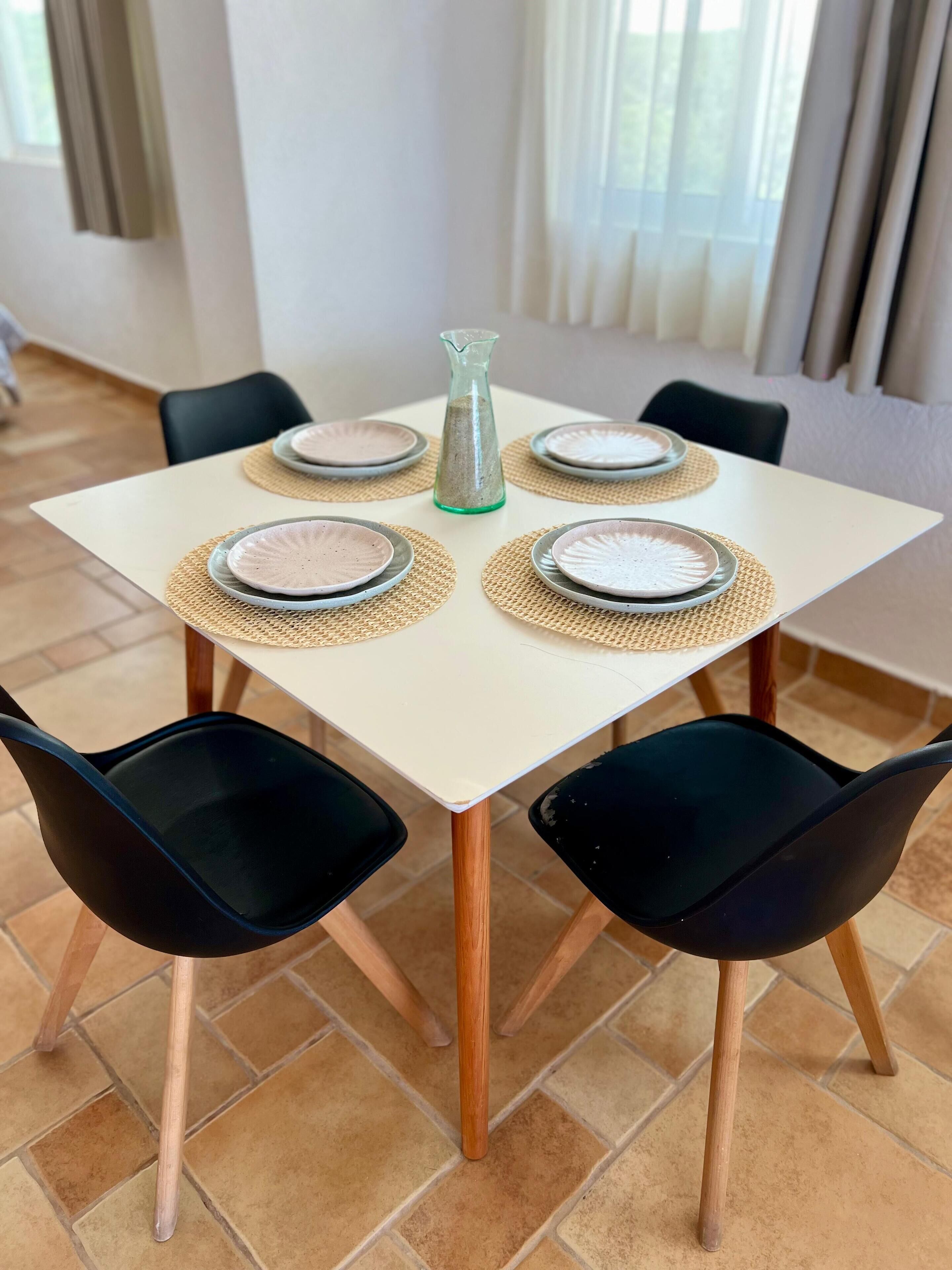 A dining table with four plates, a green vase, and black chairs.