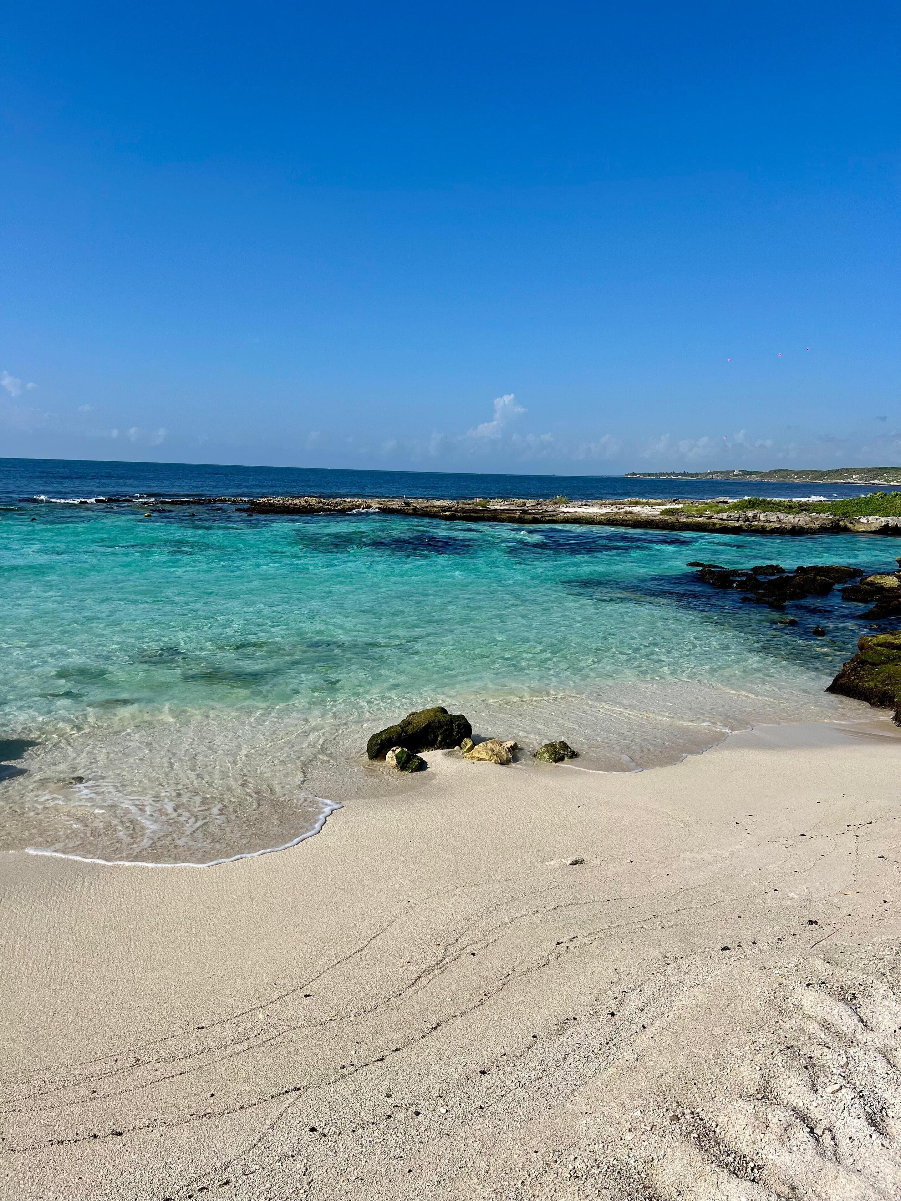 A beach with clear turquoise water, rocky outcrops, and a sandy shore.