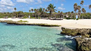 A beach with clear turquoise water, white sand, and palm trees. - Caleta Tankah (Tulum)