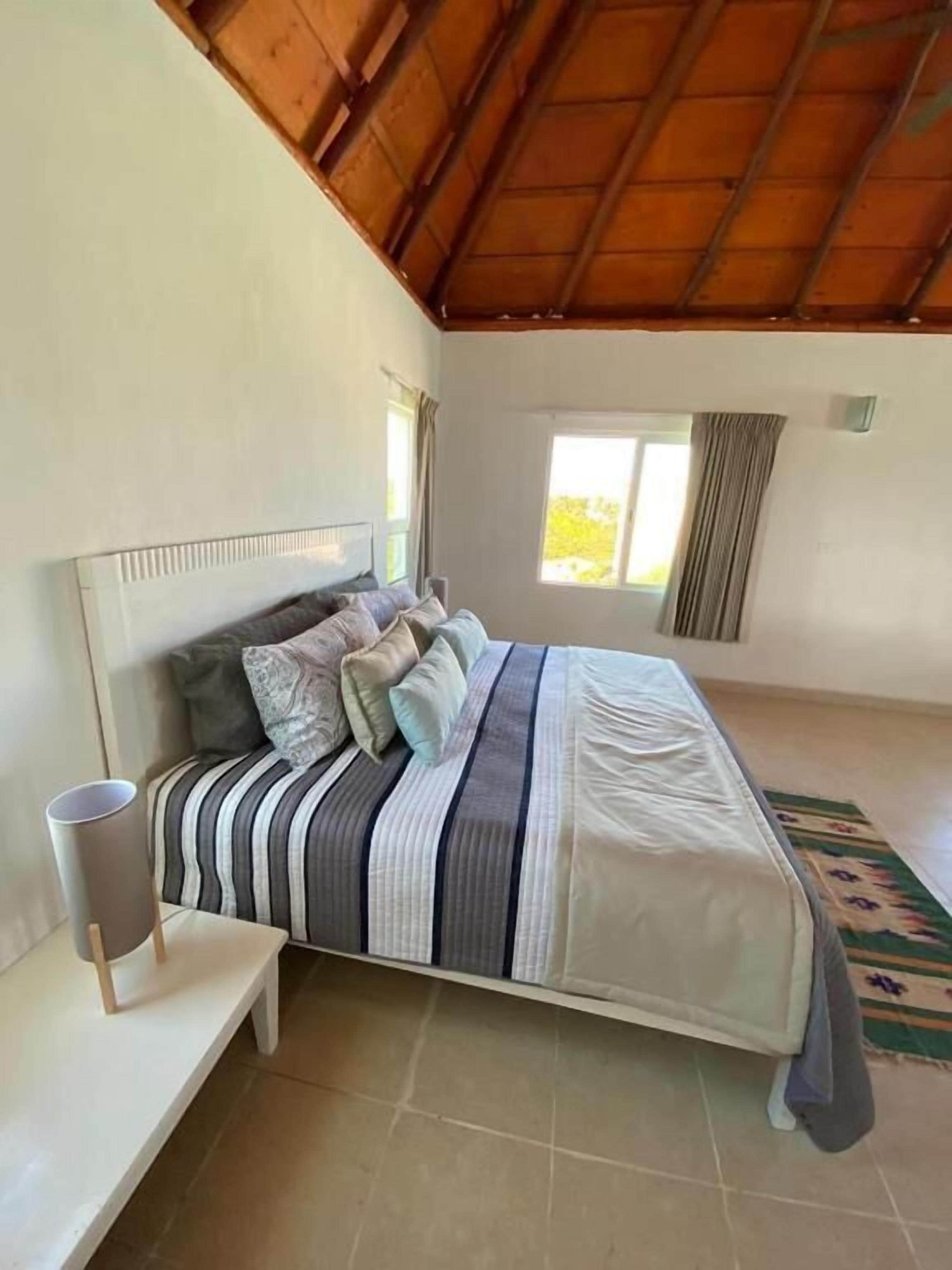A bedroom with a bed, a bedside table, a window, and a view of the outdoors.