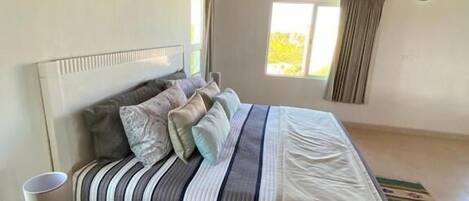 A bedroom with a bed, a bedside table, a window, and a view of the outdoors.