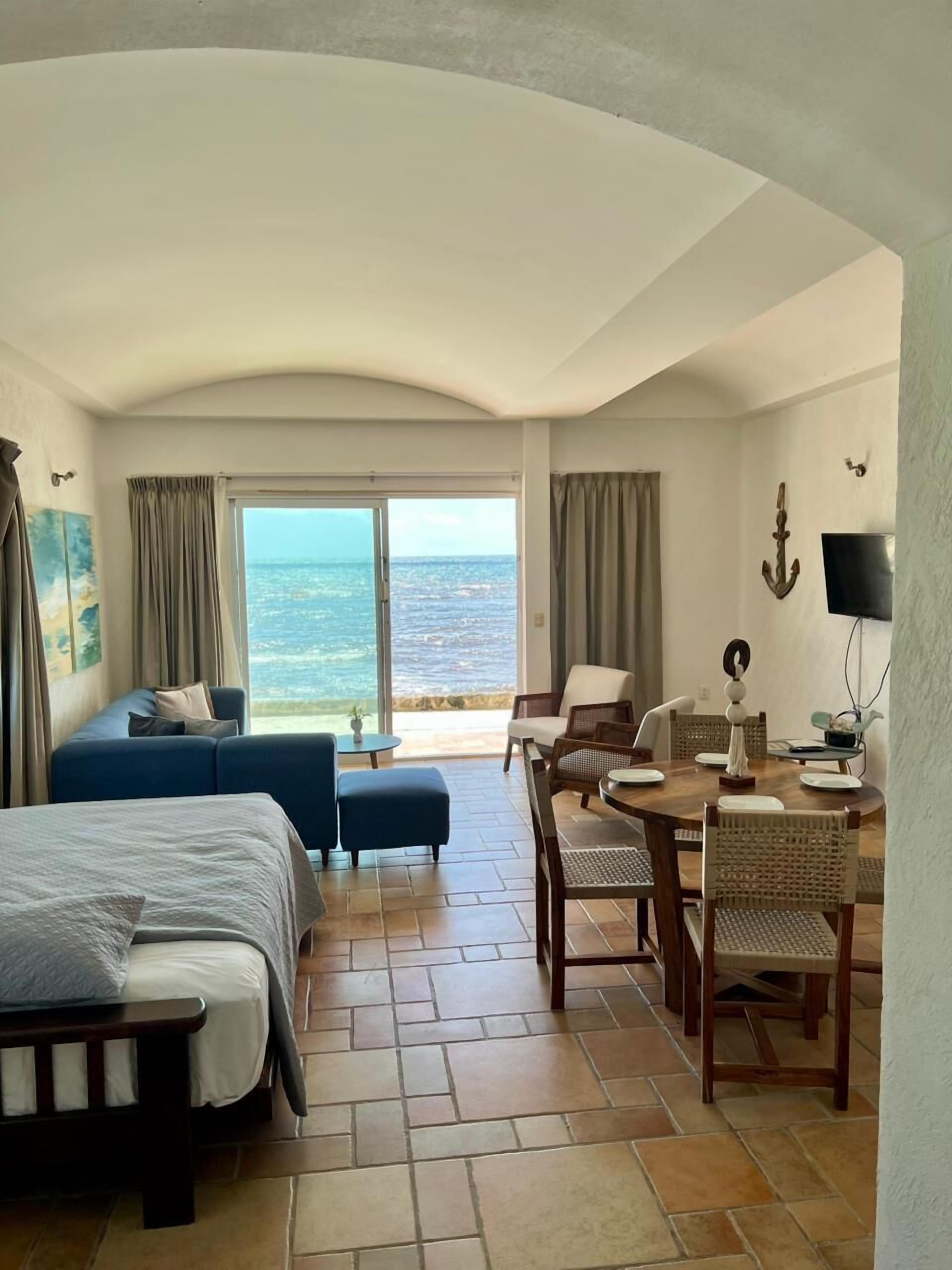 A hotel room with a bed, a seating area with a table and chairs, a TV, and a view of the ocean.