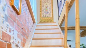 Un escalier avec des marches en bois et une rampe, menant à une pièce dont un mur est en briques et qui contient un tableau encadré.
