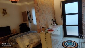 Une chambre à coucher avec un lit, une commode, un téléviseur et une fenêtre avec des stores.