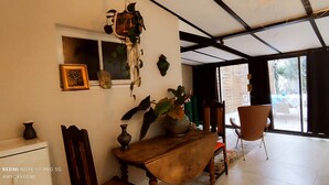 Une pièce avec une table en bois, des chaises, une plante suspendue et une fenêtre donnant sur l’extérieur.