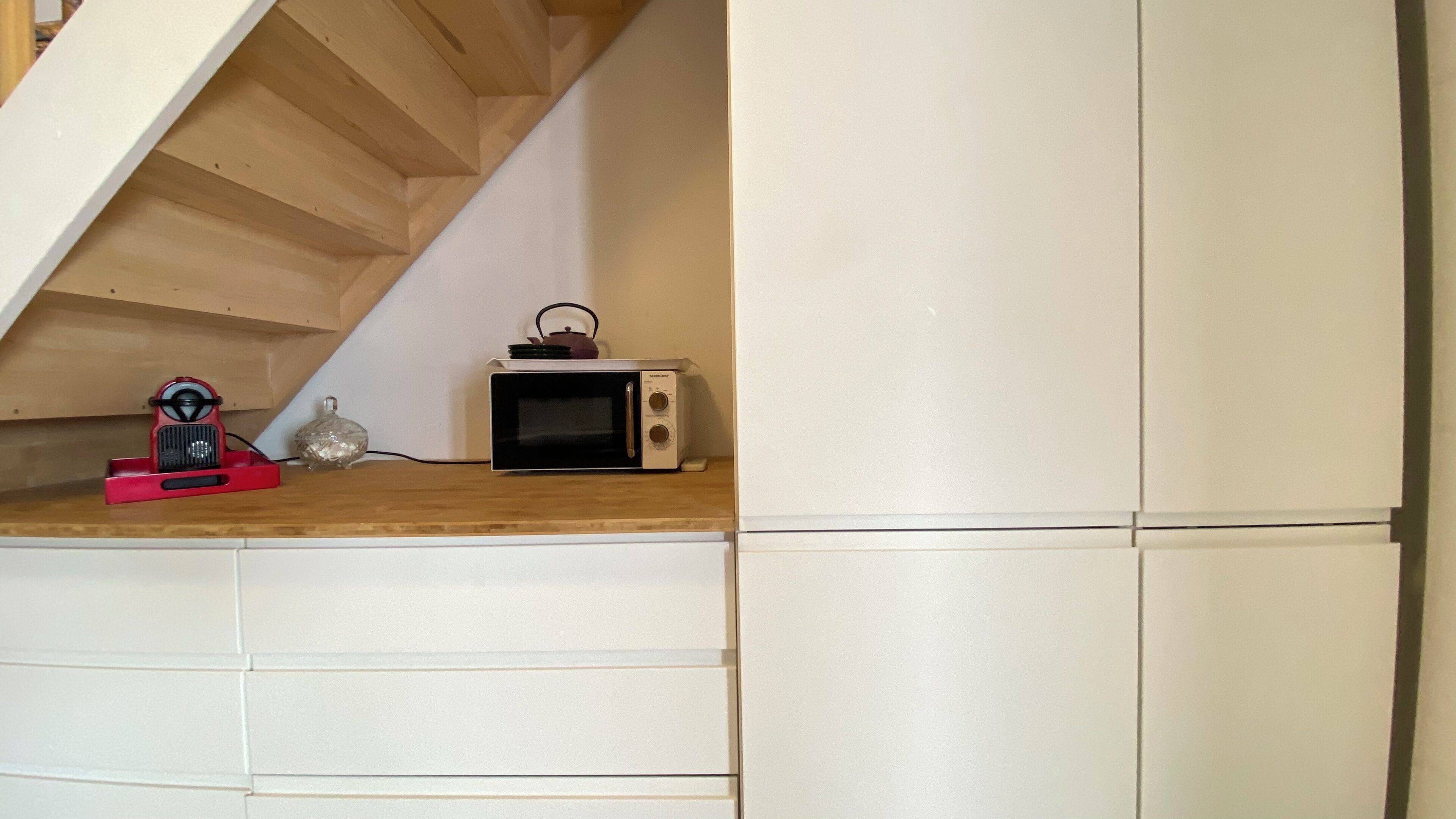 A small kitchenette with a microwave and a red appliance on a wooden shelf.