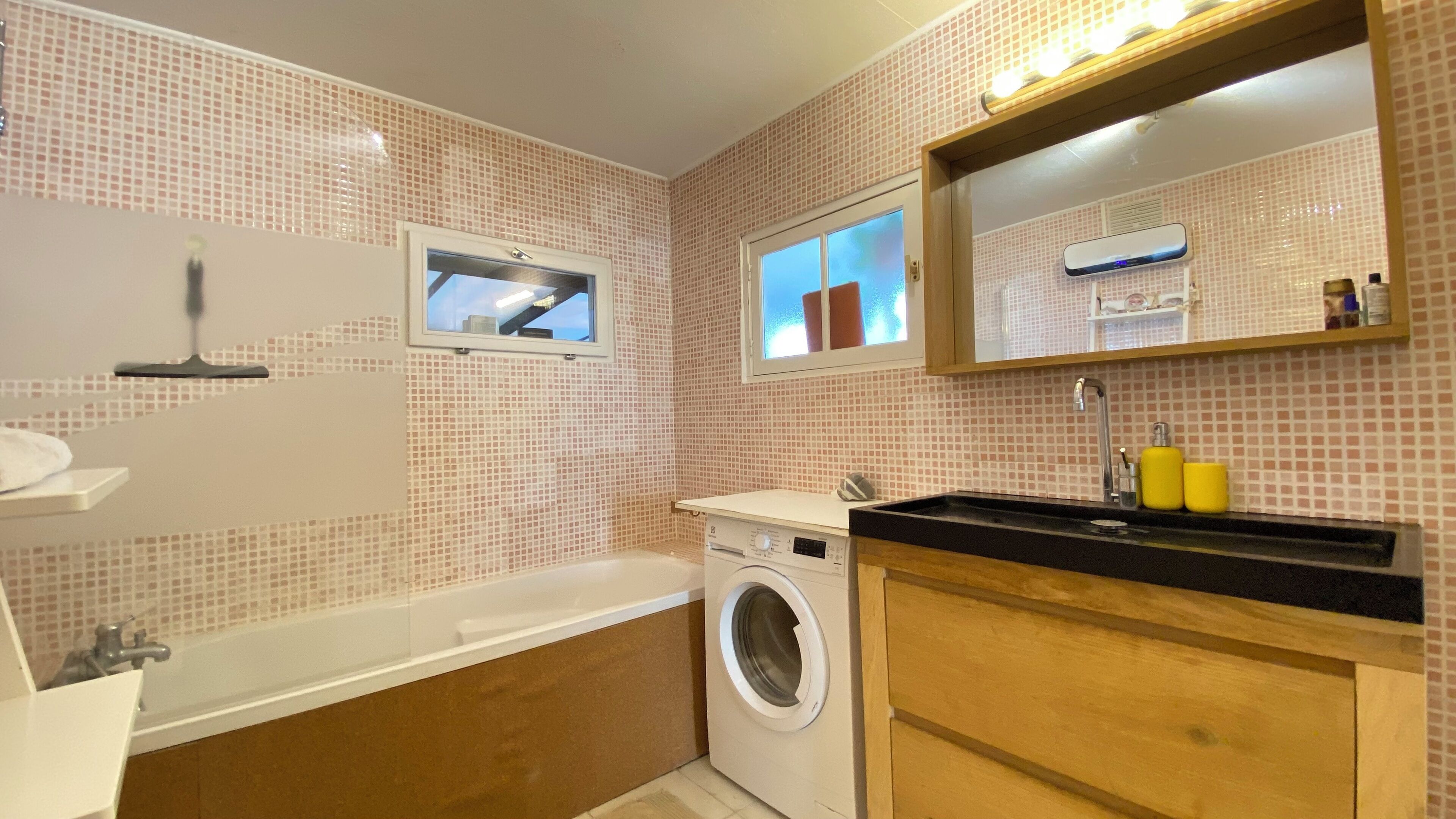 A compact bathroom with a washing machine, a bathtub, and a sink with a mirror above.