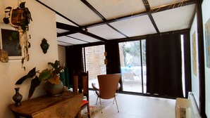 A room with a wooden table, chairs, a hanging plant, and a window with a view of the outside.
