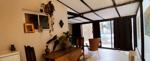 A room with a wooden table, chairs, a hanging plant, and a window with a view of the outside.