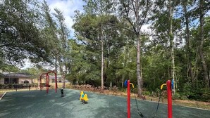 Un patio de juegos al aire libre con diversos equipos, rodeado de árboles y un edificio en el fondo.
