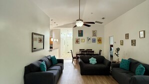 Un salón amplio con dos sofás oscuros, un ventilador de techo y una zona de comedor al fondo.