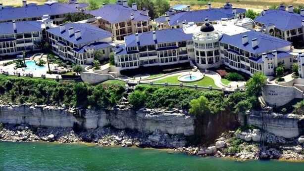 A large resort with multiple buildings, a central pool, and a rocky shoreline. - Hill Country Island Retreat - Loaded With Amenities! (Leander)