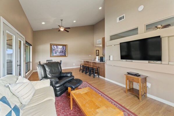 A living room with a sofa, a coffee table, a TV, and a dining area with chairs and a table. - Chardonnay Haus - Unit C (Leander)