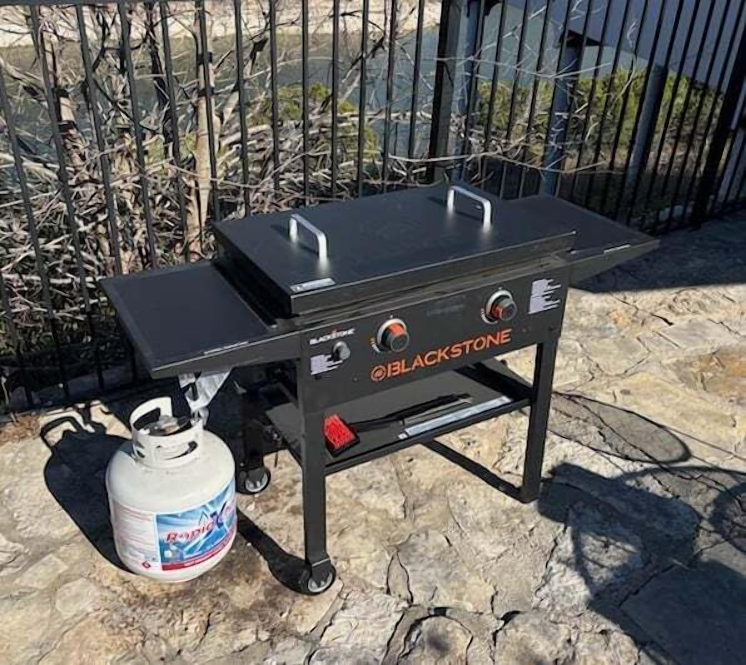 A portable gas grill with the brand name 'BLACKSTONE' and a propane tank beside it.