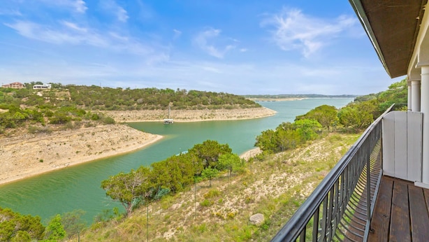 Un balcone con vista su un fiume e una barca, immerso nel verde sotto un cielo sereno.