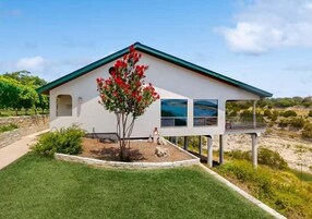 Una casa moderna con fachada blanca y tejado verde, un pequeño jardín con un árbol y vistas al paisaje.