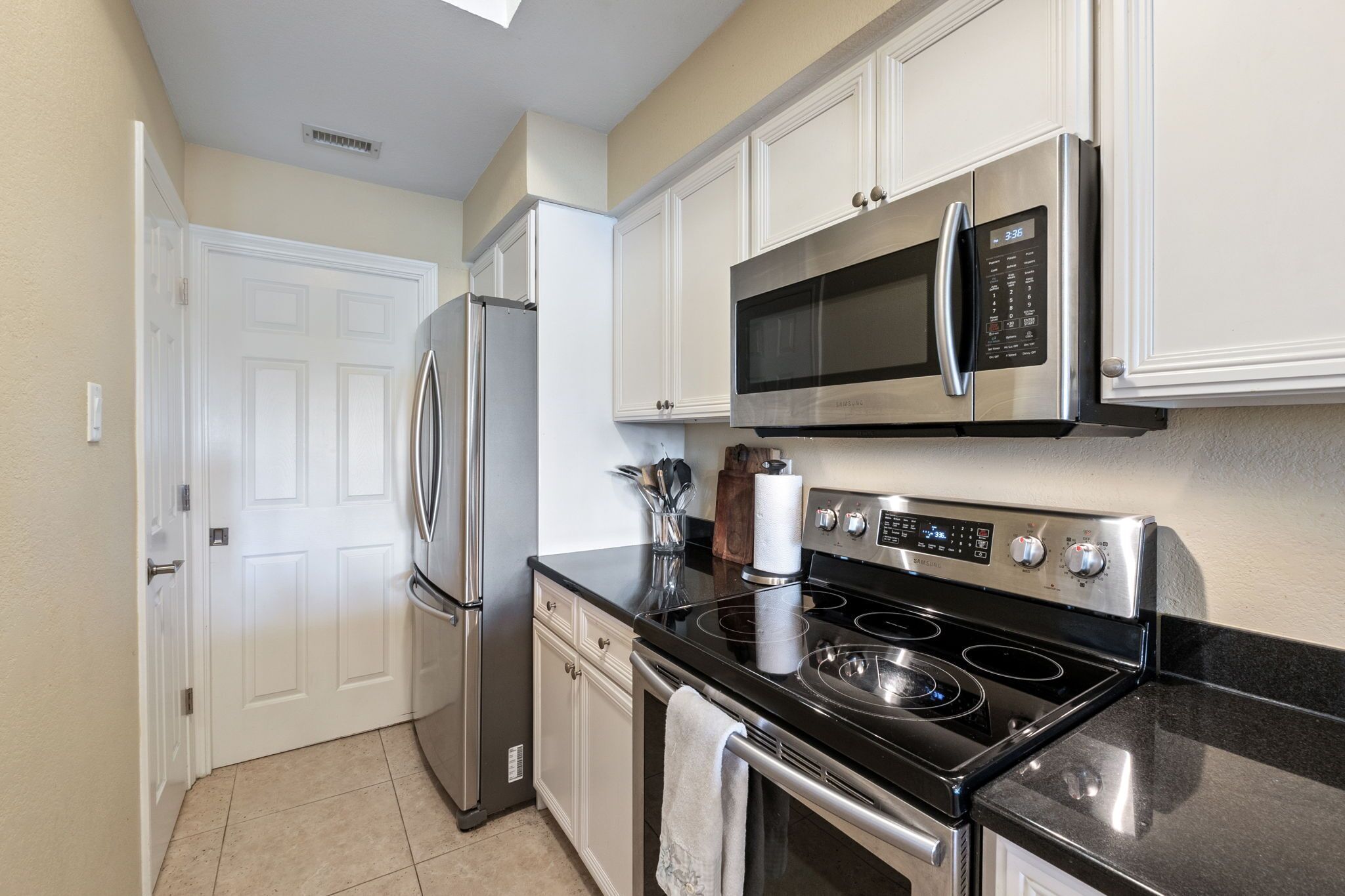 A modern kitchen with stainless steel appliances, white cabinetry, and a black countertop.