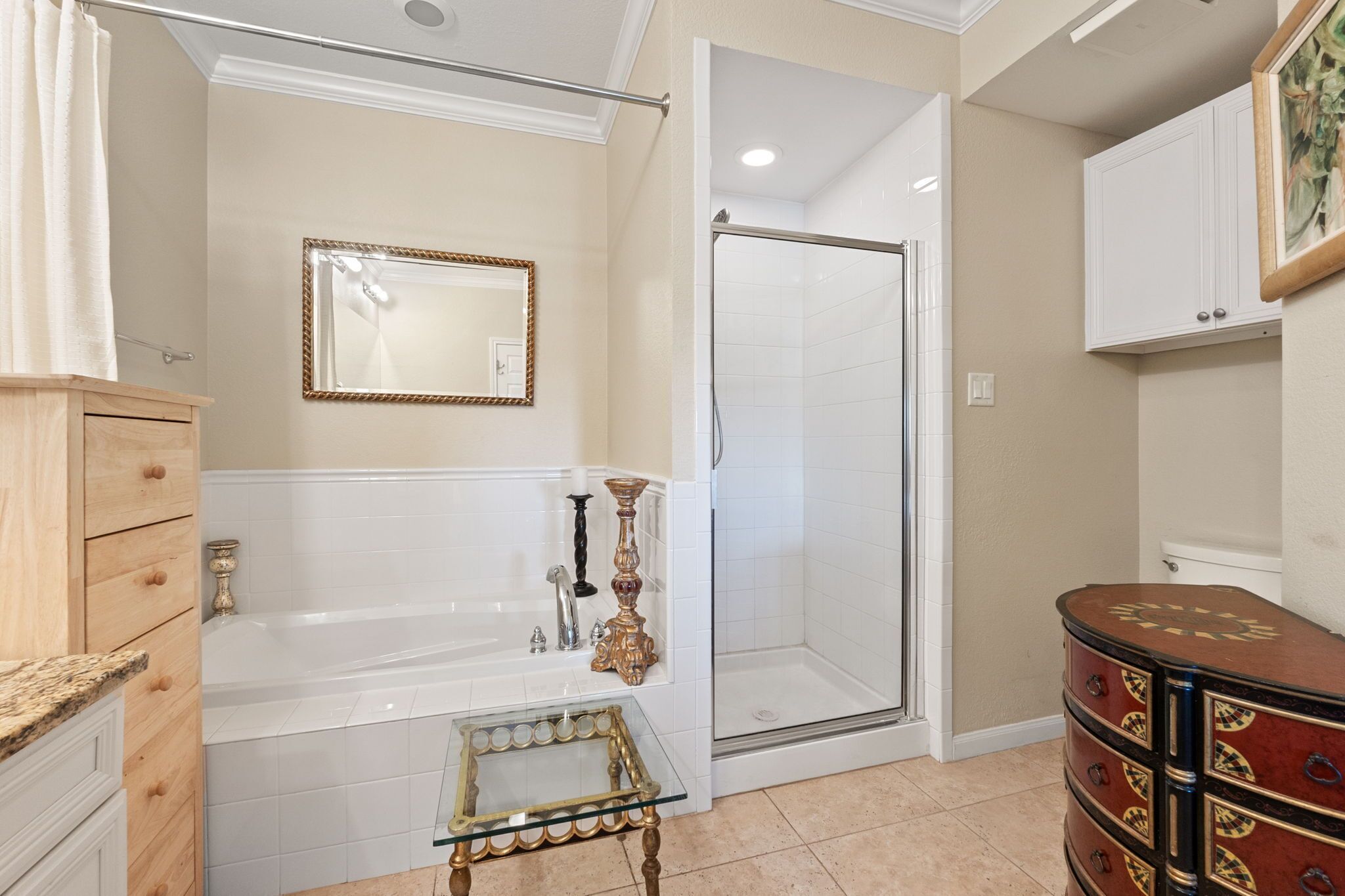 A bathroom with a bathtub, a glass-enclosed shower, a vanity with drawers, and a decorative table.