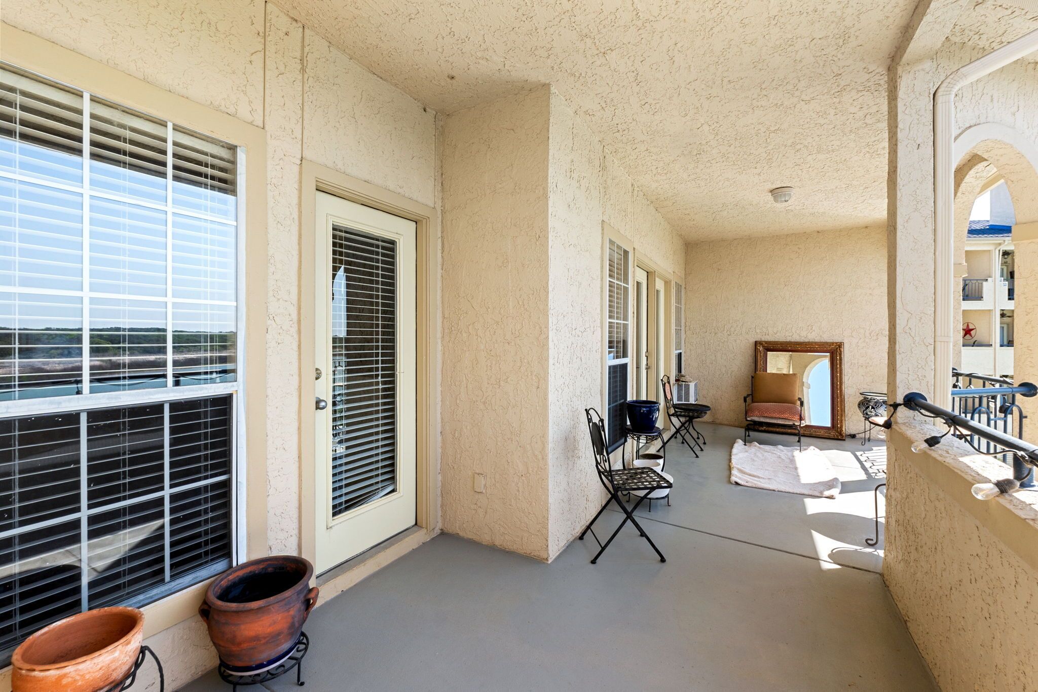 A covered balcony with a view of the landscape, a chair, a table, and a large mirror.