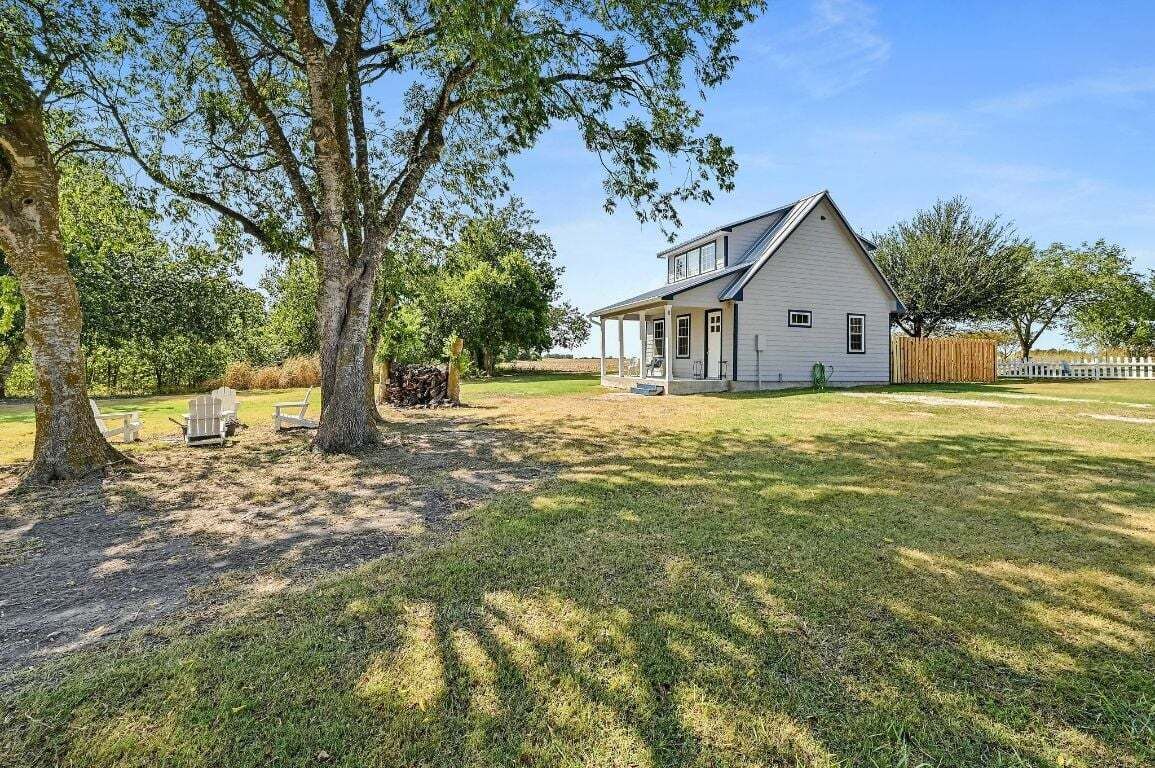 A house with a large lawn, a covered porch, and a wooden fence in the background.