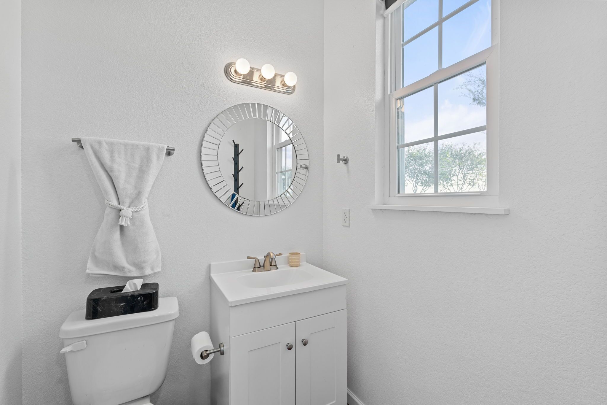Ein Badezimmer mit Toilette, Waschbecken, Spiegel und einem Fenster mit Blick auf Bäume.