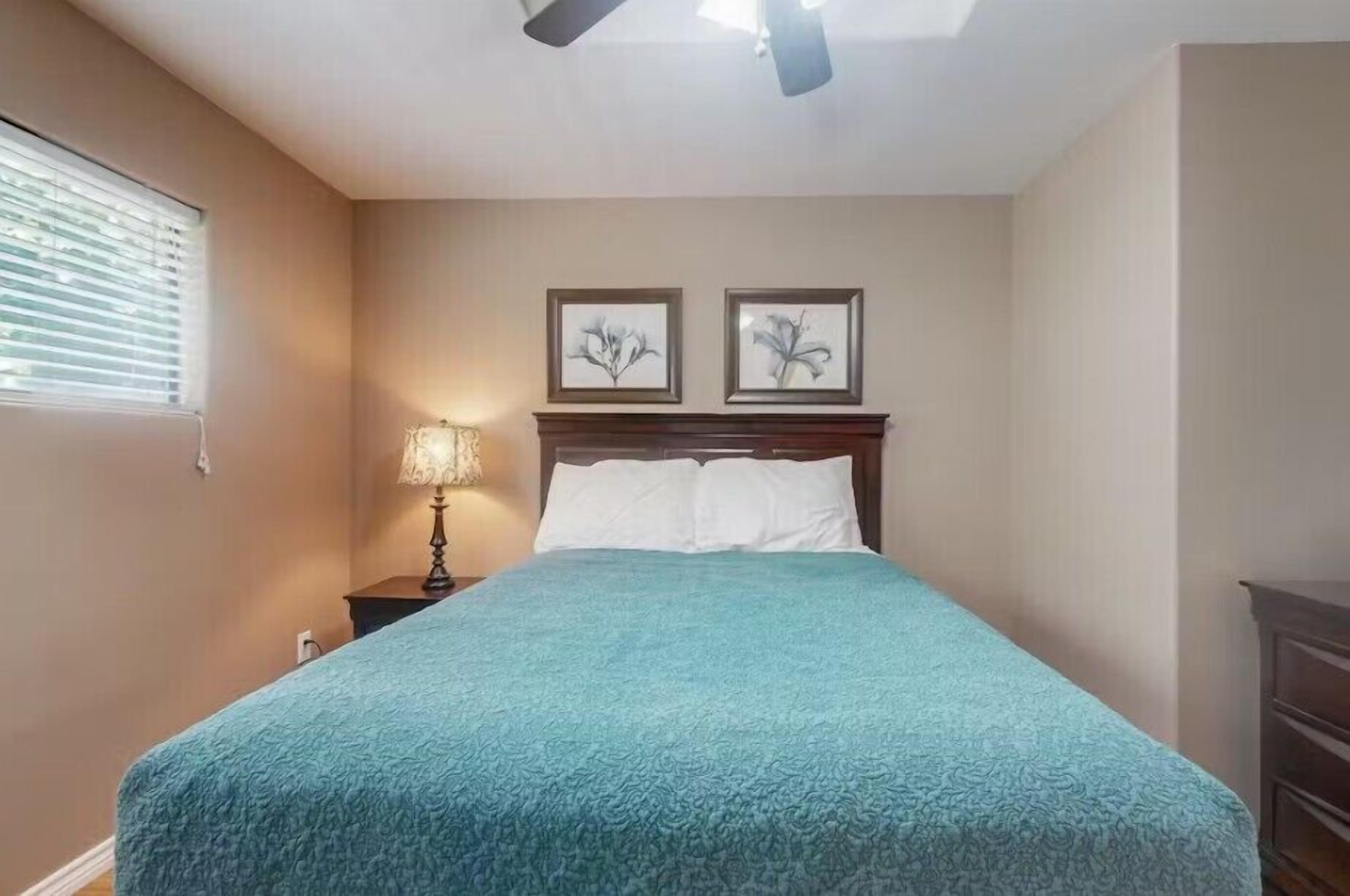 Ein Schlafzimmer mit einem Bett, einem Nachttisch, einer Lampe und zwei an der Wand befestigten Bildern.