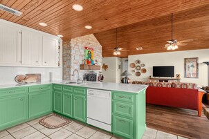 Una cocina con gabinetes verdes, lavavajillas y una pared de piedra.
