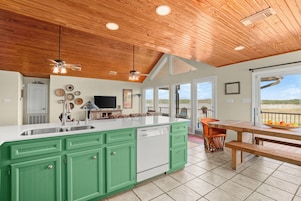 Una cocina con armarios verdes, lavavajillas e isla grande. Hay una zona de comedor con mesa y sillas de madera.