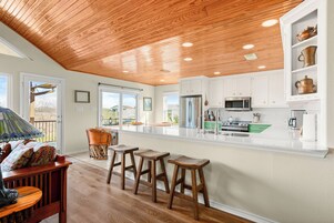 Una cocina moderna con techo de madera, gabinetes blancos y una isla grande con taburetes.