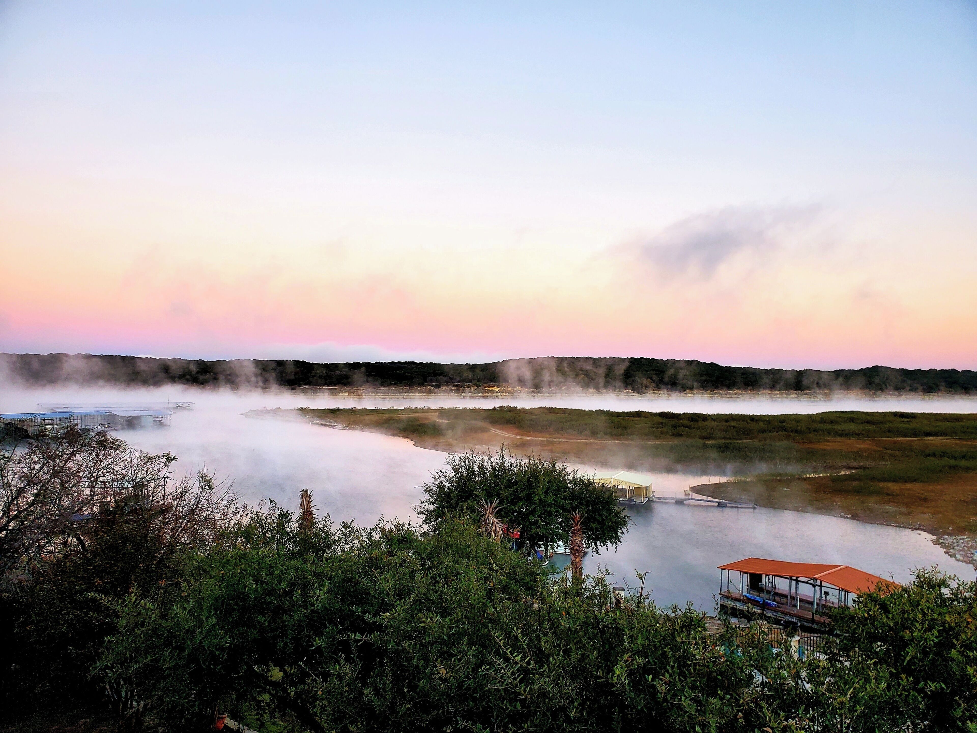 A natural landscape with a body of water, steam rising from the surface, and a distant hill.