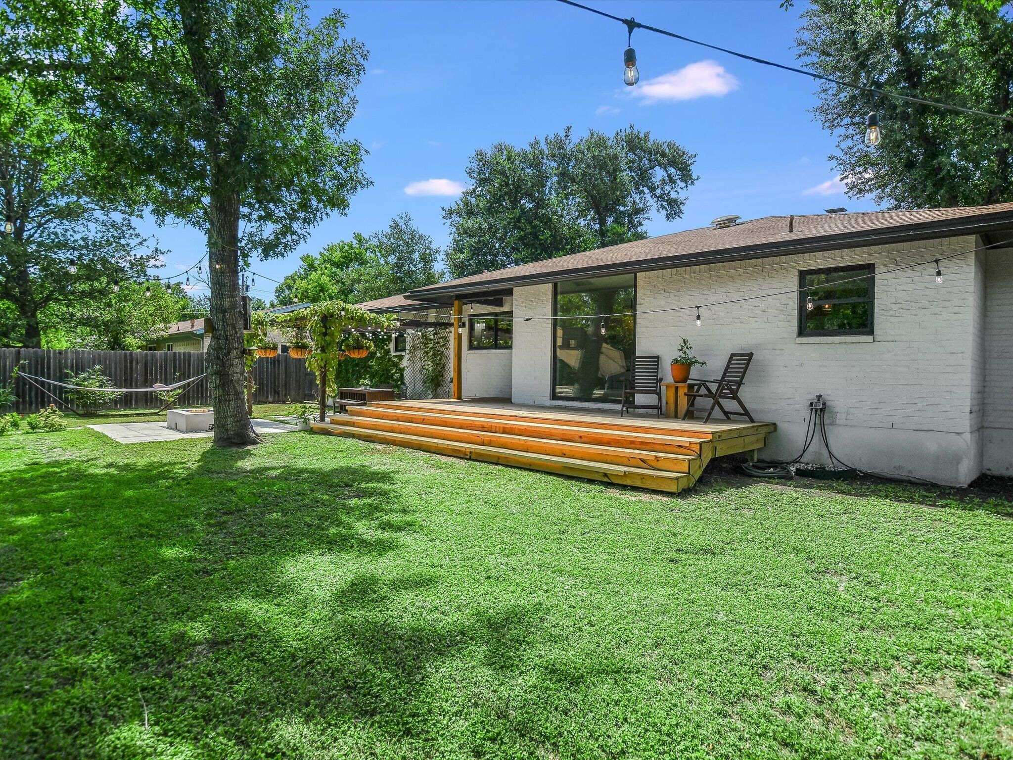 Une maison de plain-pied dotée d’une terrasse en bois, d’une porte-fenêtre coulissante et d’un petit espace patio avec deux chaises et une table.