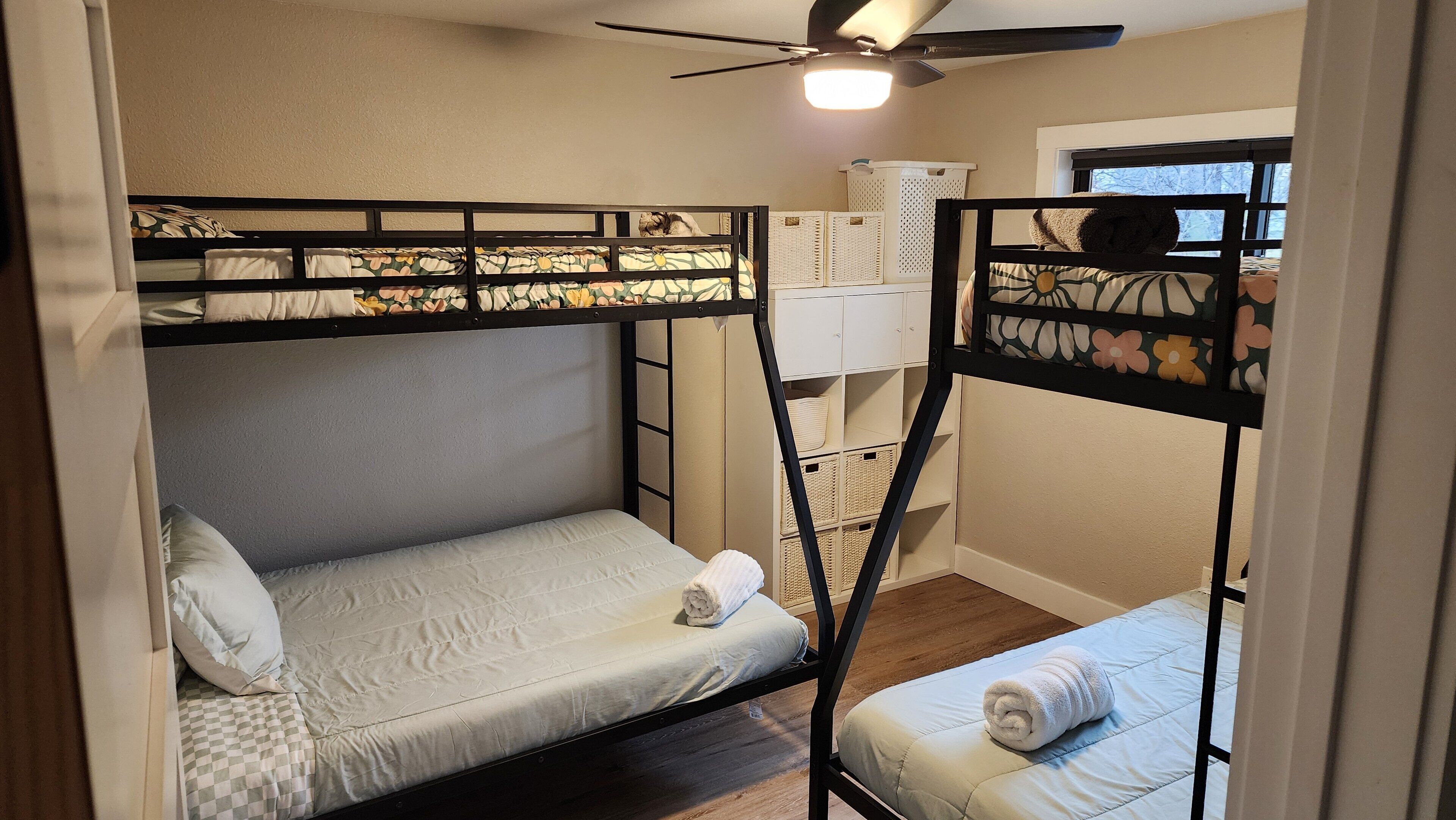 Een slaapkamer met stapelbed, plafondventilator, raam met uitzicht en opbergkasten.