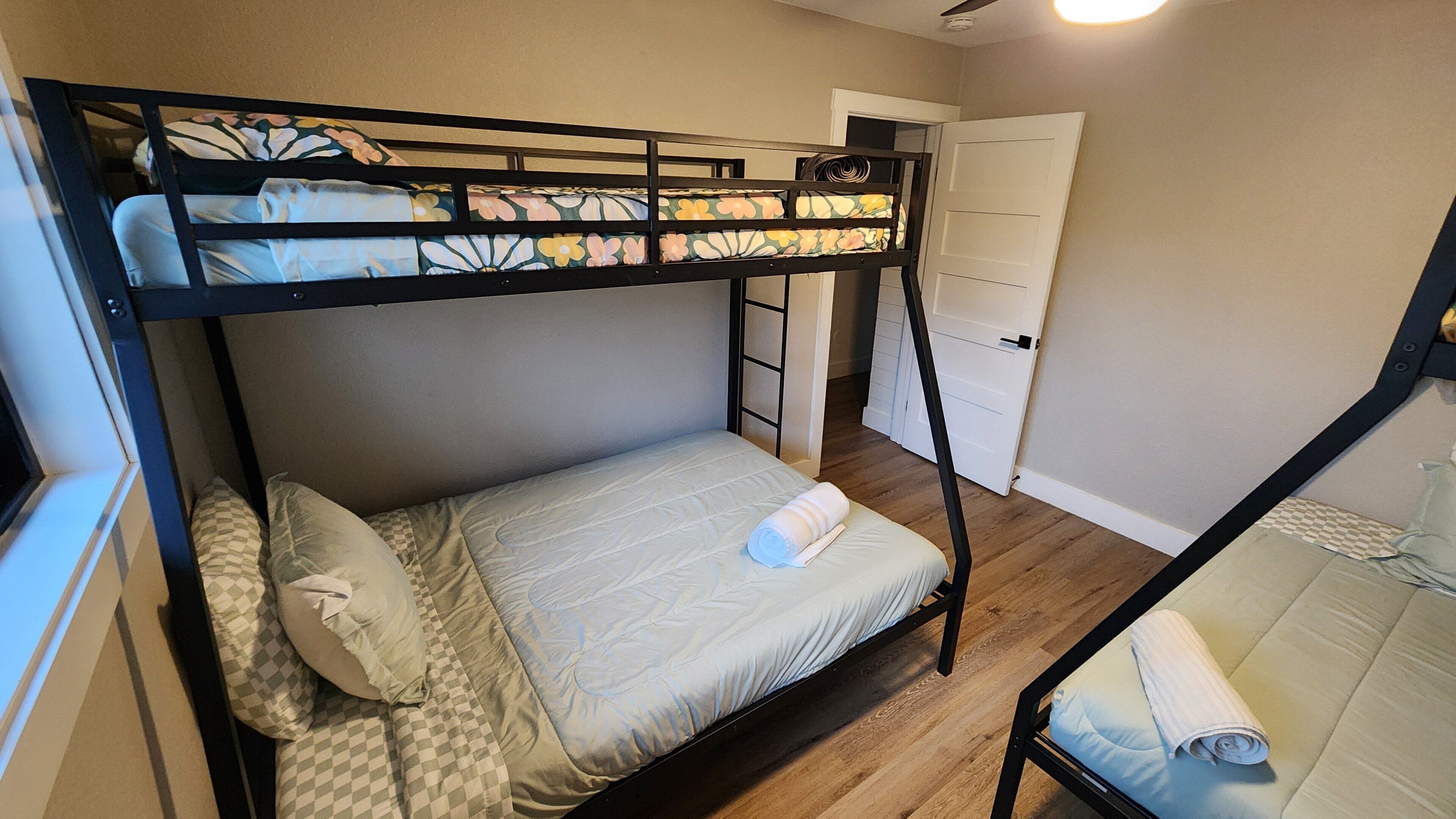 Habitación con literas, un cojín a cuadros, una toalla enrollada y una escalera que lleva a una puerta.