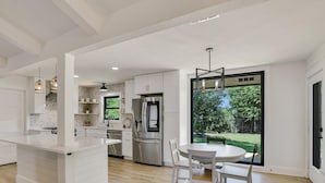 A modern kitchen with white cabinetry, a stainless steel refrigerator, and a dining area with a round table and chairs. - Charming Ranch Home Near Dell With Cocktail Pool (Round Rock)
