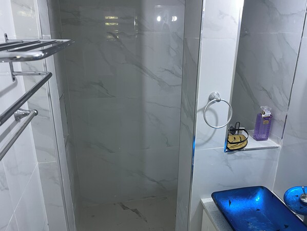 Ein Badezimmer mit Duschkabine, Handtuchhalter, Seifenspender und einem blauen Waschbecken.