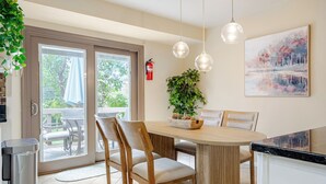 Una cocina moderna con una mesa de comedor de madera, sillas, lámparas colgantes, una planta en maceta y un extintor.