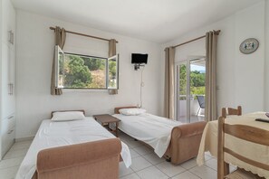 A hotel room with two beds, a TV, a table, and a view of the outdoors.