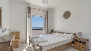 A bedroom with a wooden bed, a desk, a chair, a bedside table, and a view of the sea through an open window. - Apartment '1 Bedroom  with Balcony 5' with Sea View, Wi-Fi and Air Conditioning (Spartià)