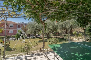 Un jardín con un columpio, una mesa verde y una pérgola.