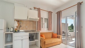 Une cuisine compacte équipée d’un four encastré, d’une machine à café et d’un évier. On y trouve également un canapé et une table à manger avec des chaises.