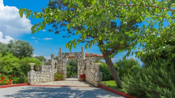 Un arc en pierre mène à un jardin sous un ciel dégagé.