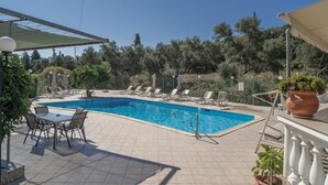 A swimming pool with lounge chairs and a table, surrounded by greenery and a clear sky.