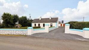 A two-story house with a stone wall and a blue-painted gate. - Tig Davy (Mullagh)