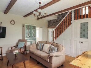 A cozy living room with a wooden staircase, a beige sofa, a wooden coffee table, and a TV mounted on the wall. - Tig Davy (Mullagh)