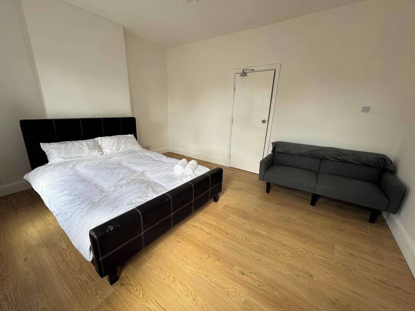 A bedroom with a bed, a grey sofa, and a door.