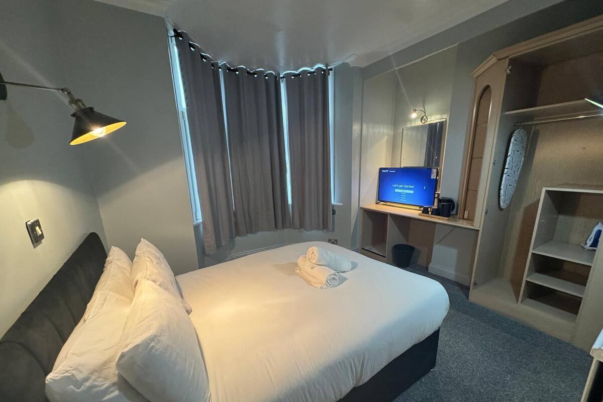 A hotel room with a bed, a desk with a computer, a wardrobe, and a shower area.