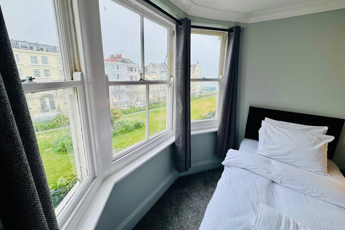 A hotel room with a large window, a neatly made bed, and a view of the cityscape.